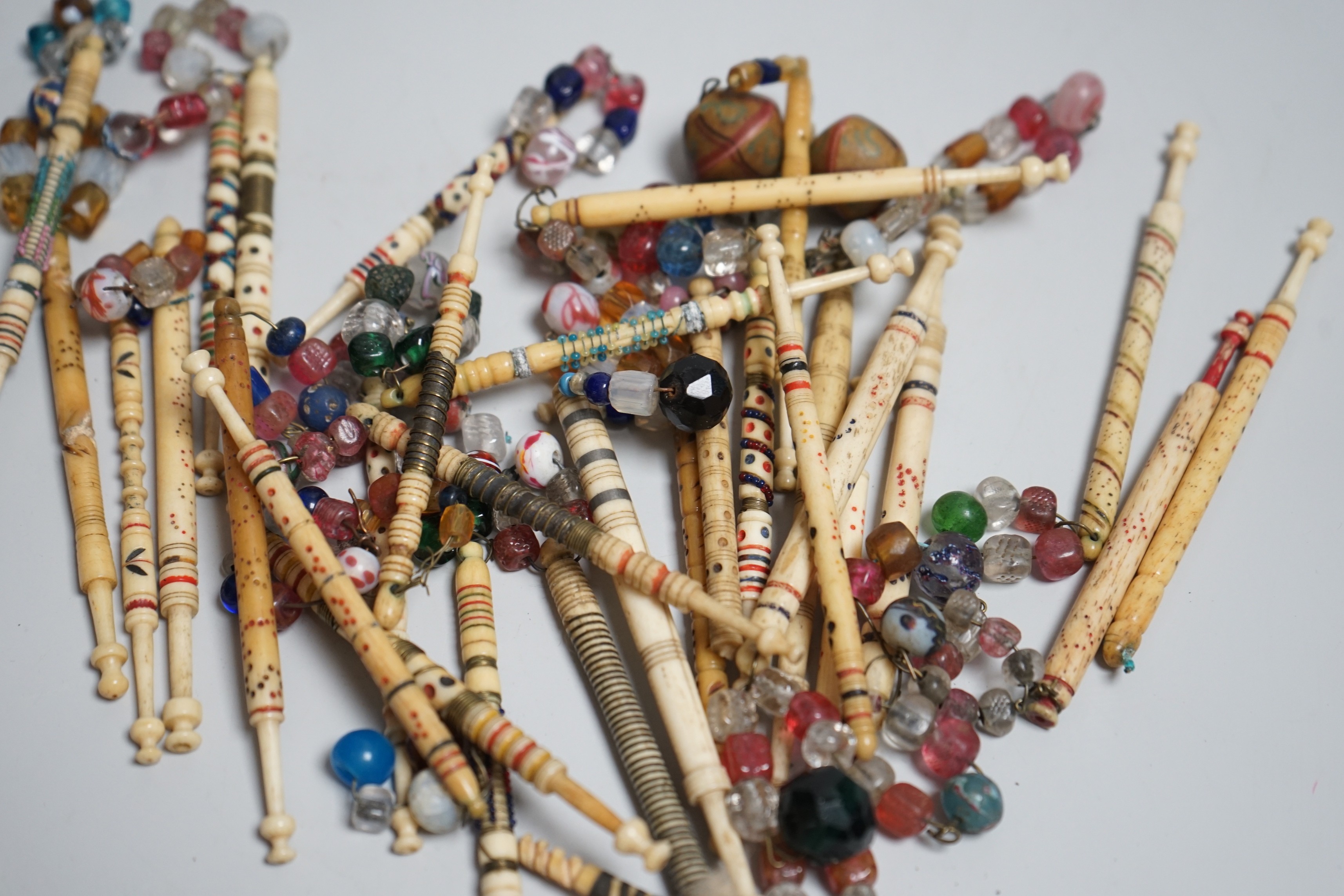 Twenty 19th century ornately decorated lace bobbins with glass bead tops and eleven carved bobbins with indistinctly carved surnames and names